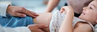 A child smiles while receiving an abdominal checkup from a pediatric gastroenterologist.